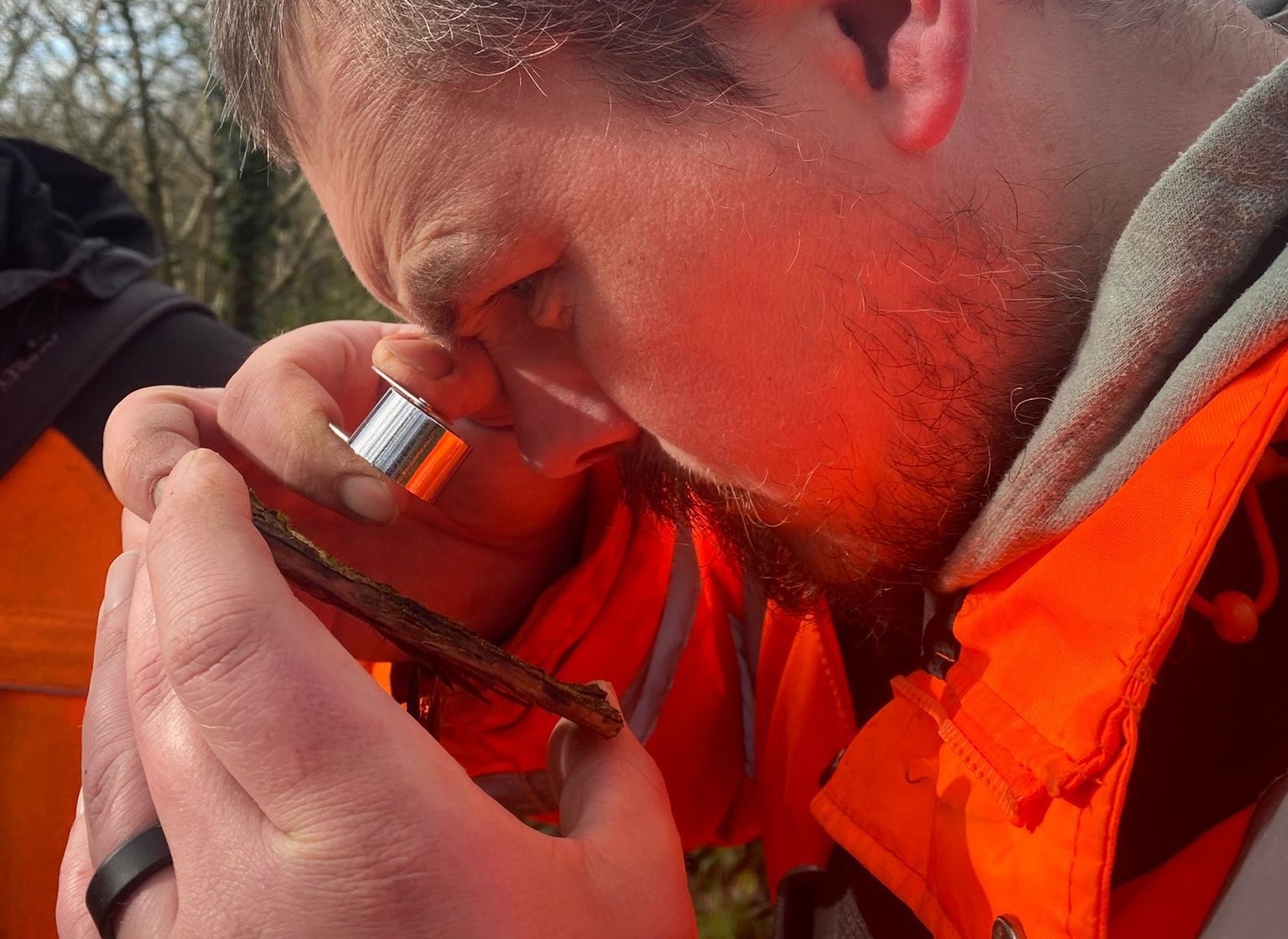 Close-up of a man in an orange jacket bringing a small metallic container to his nose outdoors